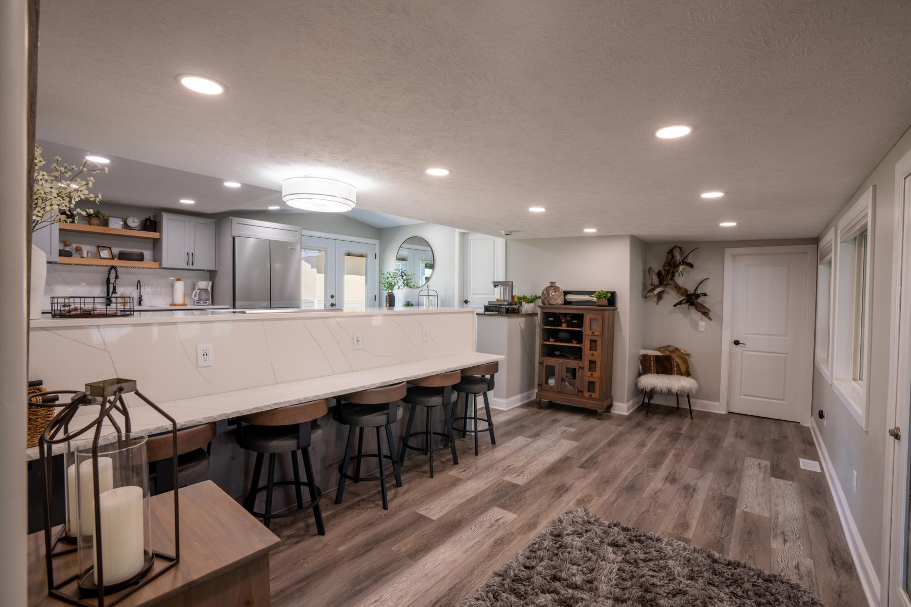 nebraska-waterfowl-hunting-lodge11 - Xtreme Waterfowlers - Nebraska Guided Duck & Goose Hunts Modern basement kitchen with a white marble island, gray cabinetry, stainless fridge, and row of bar stools along the island